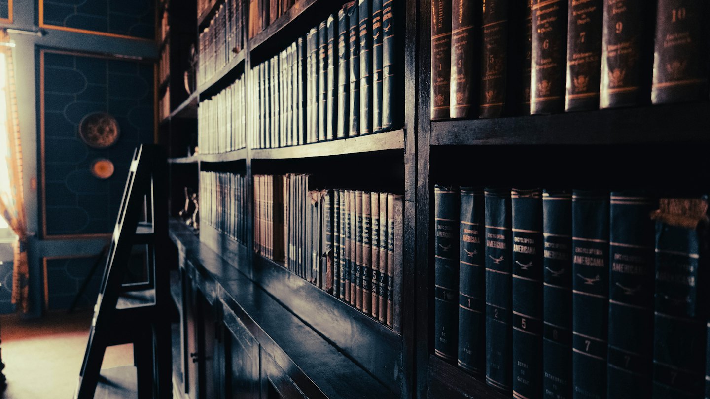 Antique books line the wooden shelves of a library.