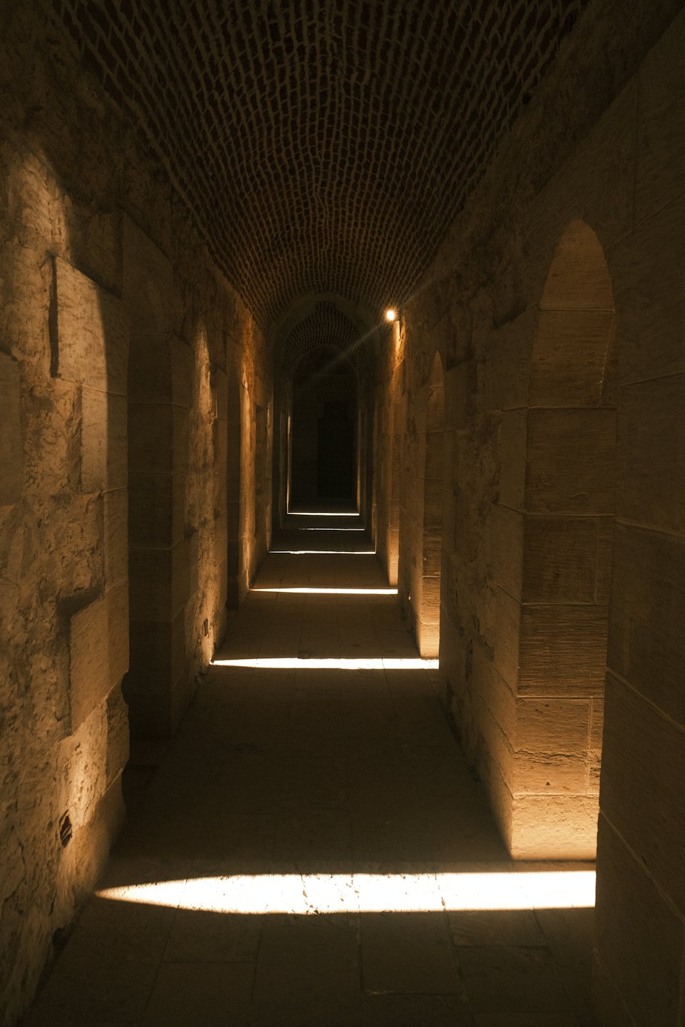 Sunlight shines through arches into a long stone corridor.