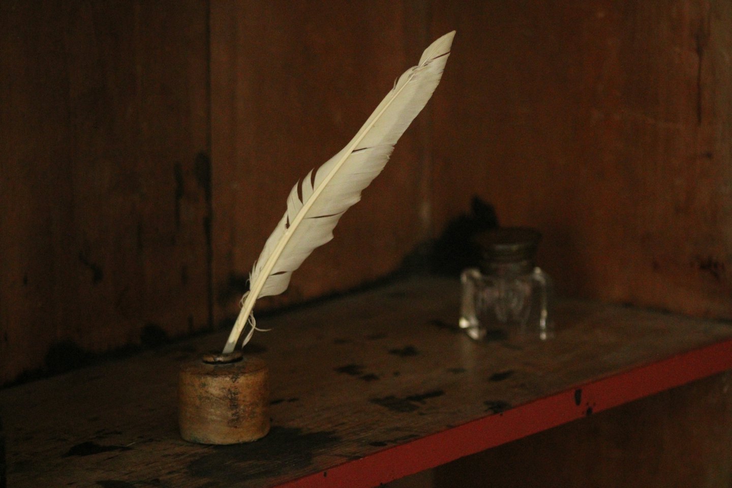 A white quill pen rests inside a rustic ceramic inkwell.